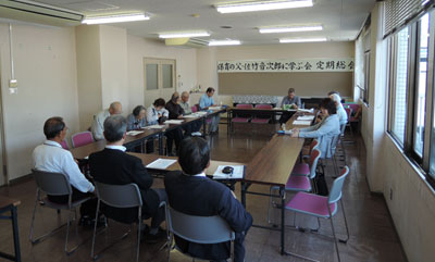 総会の様子。ロの字型に会議用テーブルが６つ並べられており３人の男性の背中から正面へ向かって撮影。右手にはブラインドが上げられて、窓も開けられ、やわらかい春の日差しとそよ風が会議室に入ってきている。