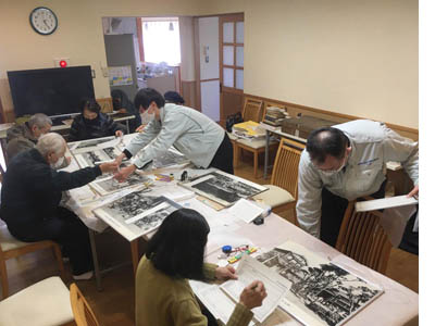 数名が史料を見ながら調査カードへ記入している様子。中央ではちょうど城博さんに渥美委員が完成した調査カードを手渡している。