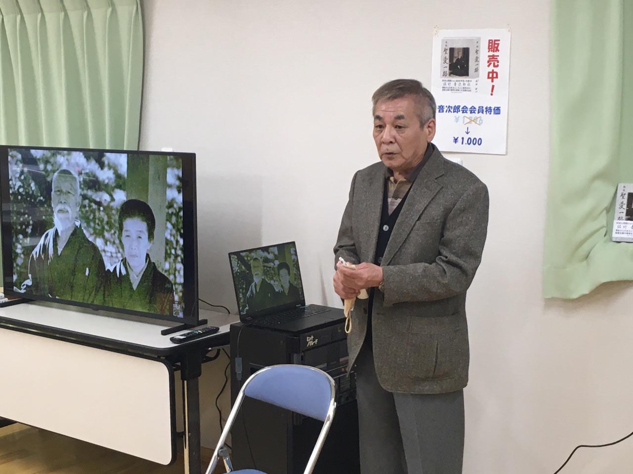 音次郎夫妻の映像を背に話をする中平会長